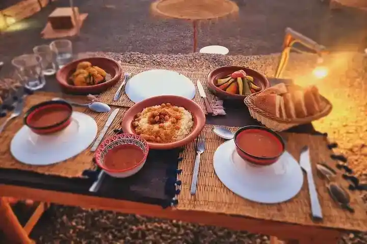 Authentic Moroccan dinner setup in the Agafay Desert at sunset with traditional dishes and warm ambiance