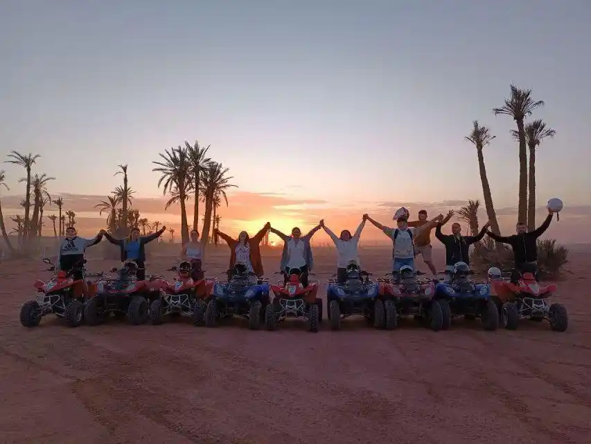 Group of tourists posing with quad bikes at sunset in the Marrakech Palmeraie palm grove.