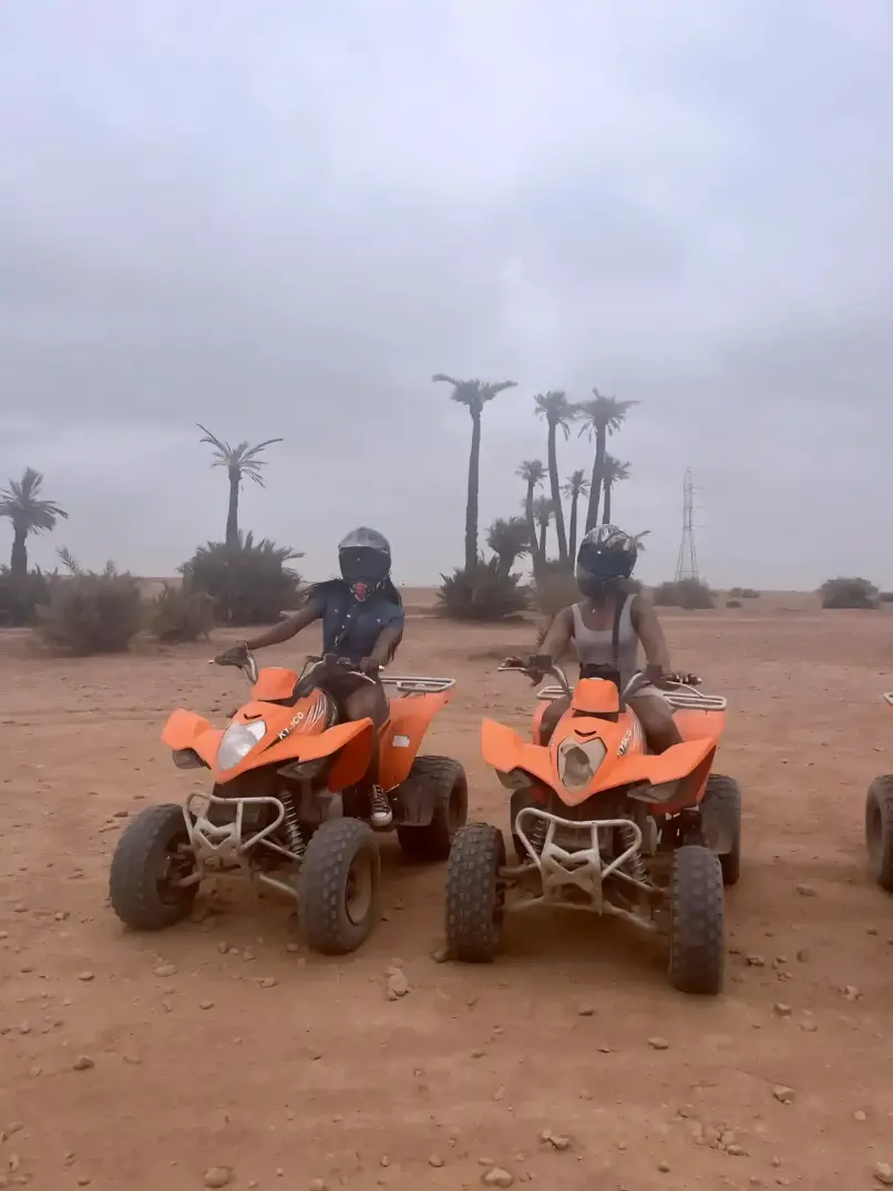 Two travelers riding orange quad bikes during a private Marrakech quad tour in the Palmeraie with hotel pickup and local guide