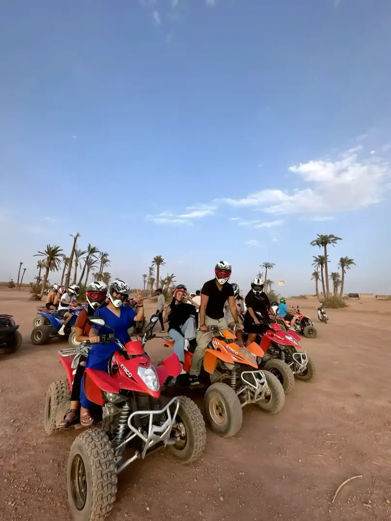 Group of tourists enjoying a private quad tour in Marrakech Palmeraie with hotel pickup, riding quad bikes through the palm grove under a blue sky