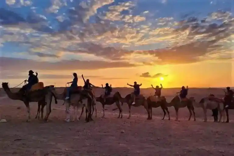 Camel caravan crossing the Agafay Desert at sunset with dramatic golden skies near Marrakech